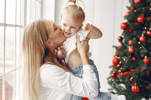 La mujer se divierte preparándose para la Navidad. Madre con camisa blanca está jugando con su hija. La familia está descansando en una sala festiva.