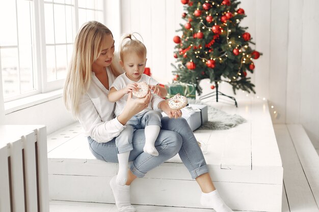 La mujer se divierte preparándose para la Navidad. Madre con camisa blanca está jugando con su hija. La familia está descansando en una sala festiva.