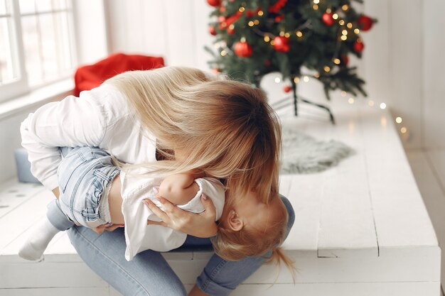 La mujer se divierte preparándose para la Navidad. Madre con camisa blanca está jugando con su hija. La familia está descansando en una sala festiva.