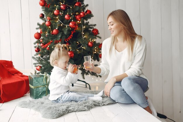 La mujer se divierte preparándose para la Navidad. Madre en suéter blanco jugando con su hija. La familia está descansando en una sala festiva.