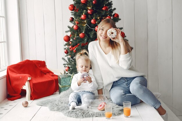 La mujer se divierte preparándose para la Navidad. Madre en suéter blanco jugando con su hija. La familia está descansando en una sala festiva.