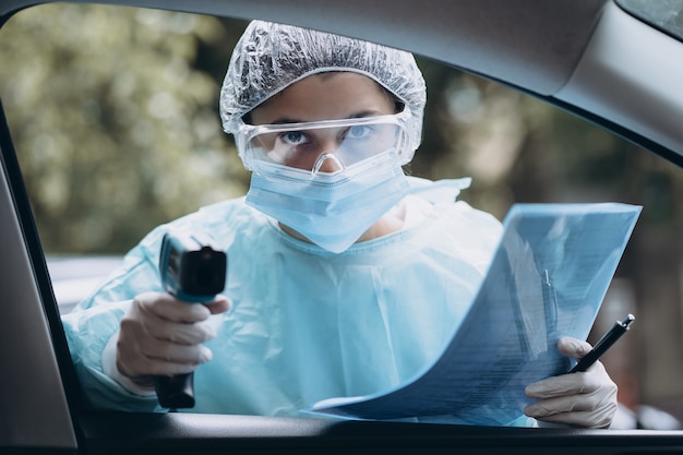 La mujer del doctor usa una pistola de termómetro infrarrojo en la frente para verificar la temperatura corporal.