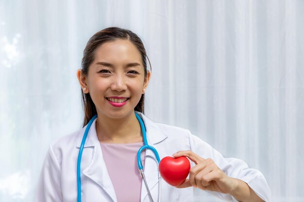 Mujer doctora con corazón rojo en la mano y diagnostica con estetoscopio