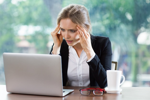 Mujer con dolor de cabeza mirando un portátil