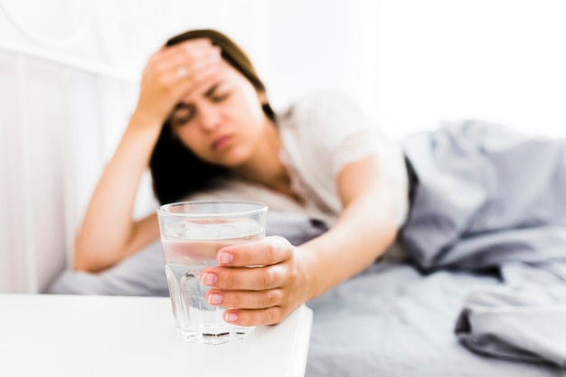 Mujer con dolor de cabeza tomando vaso de agua