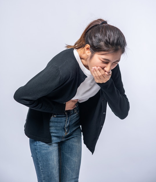 Una mujer con dolor de estómago se pone las manos sobre el estómago y se tapa la boca.