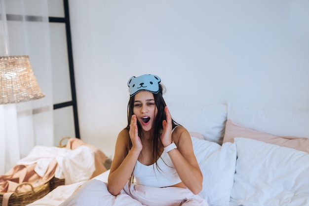 Mujer dormida despertando mientras está sentado en la cama sobre fondo blanco.