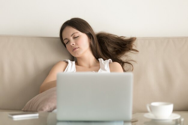 Mujer dormida en un sofá frente a una computadora portátil