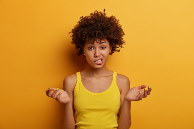 Mujer dudosa desorientada se encoge de hombros con las palmas extendidas, aprieta los dientes