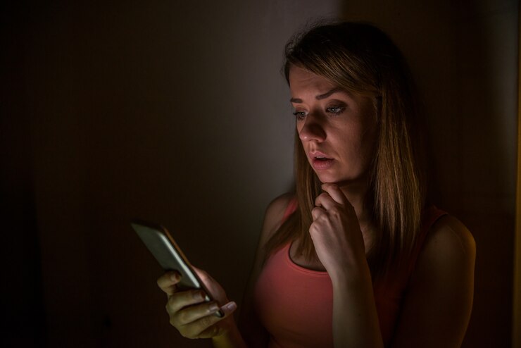 Mujer dudosa mirando hacia abajo y preguntándose si debe llamar por teléfono o esperar un mensaje