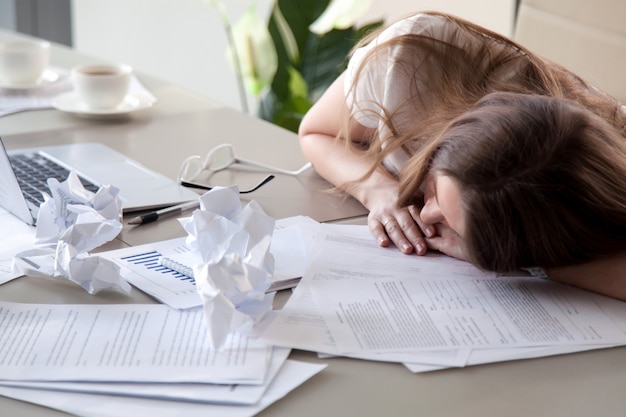 Mujer durmiendo en el escritorio cubierto de papeles arrugados