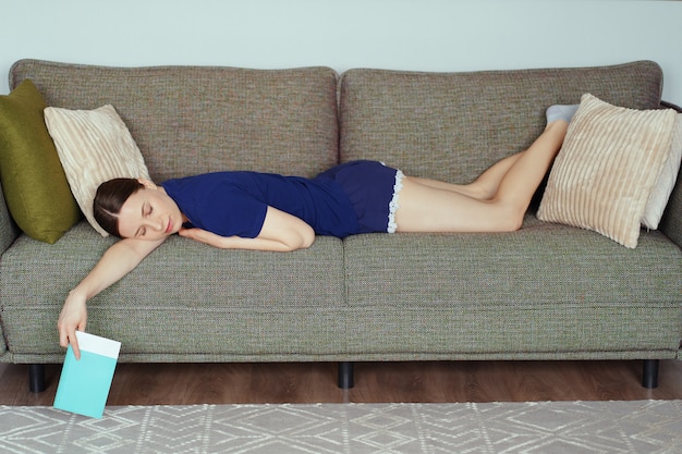 La mujer se durmió mientras leía en el sofá de la sala de estar