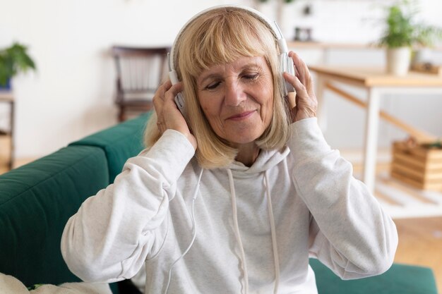 Mujer de edad avanzada con auriculares en casa escuchando música
