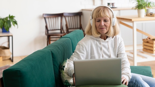 Mujer de edad avanzada en casa con auriculares y portátil
