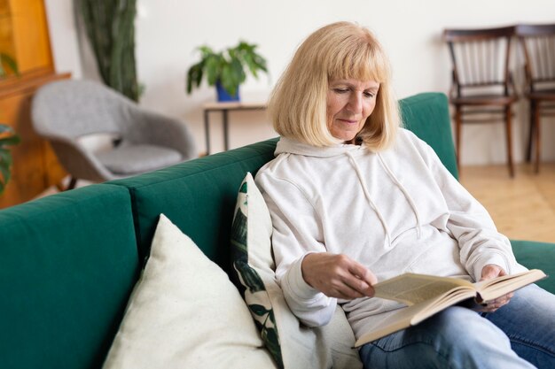 Mujer de edad avanzada en casa en el sofá leyendo un libro