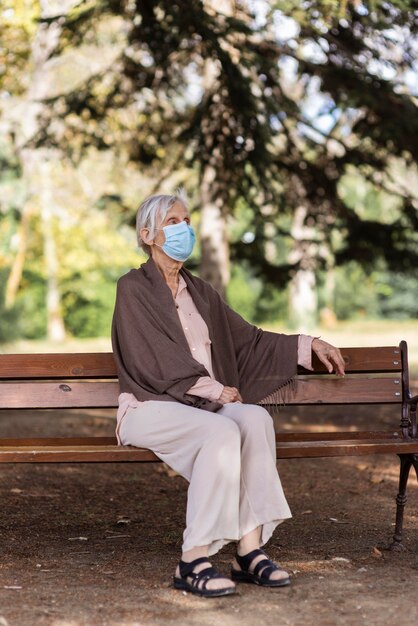 Mujer de edad avanzada con máscara médica sentado en un banco