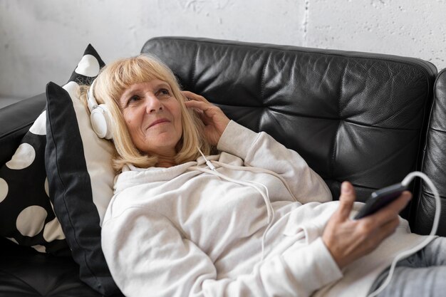 Mujer de edad avanzada en el sofá escuchando música con auriculares