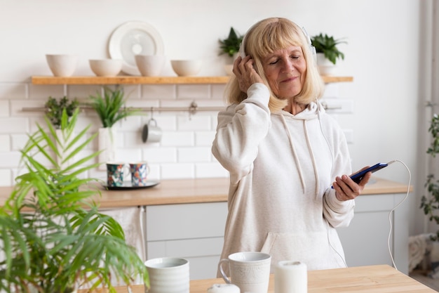 Mujer de edad escuchando música con auriculares en casa