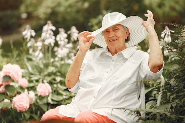 Mujer de edad sentada en el parque. Abuela con sombrero blanco.