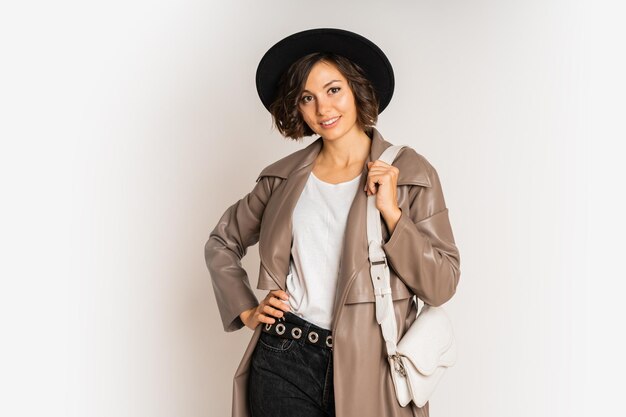 Mujer elegante con abrigo de cuero y sombrero negro demuestran las tendencias de la moda de invierno en blanco.