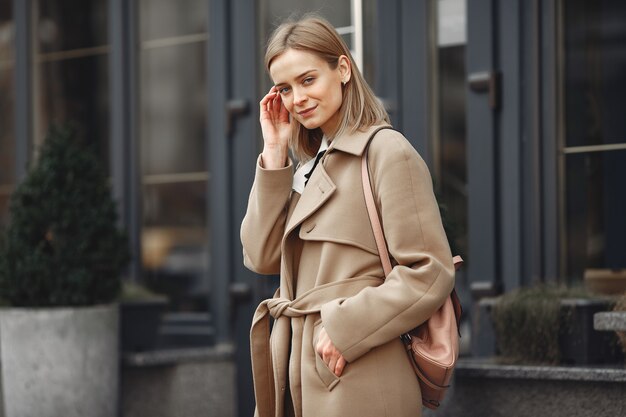 Mujer elegante con un abrigo marrón en una ciudad de primavera