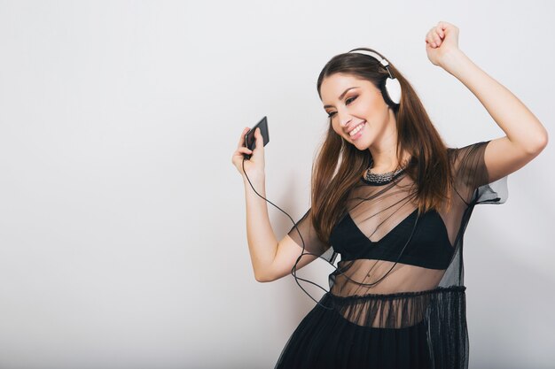 Mujer elegante aislada en traje negro escuchando música en auriculares bailando