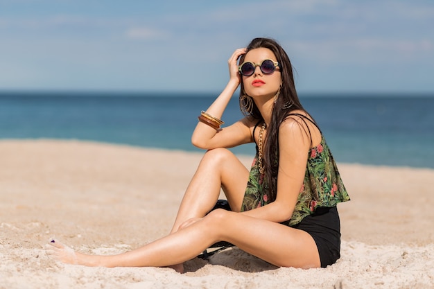 mujer en elegante autfit tropical posando en la playa.