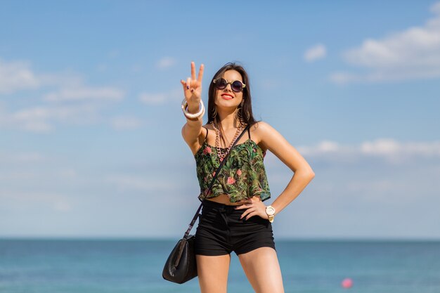 mujer en elegante autfit tropical posando en la playa.