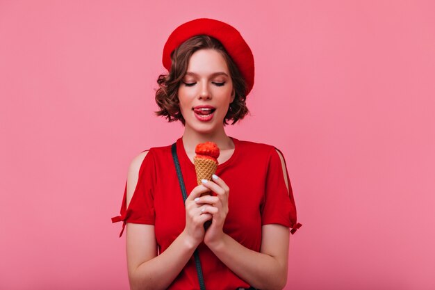 Mujer elegante bien vestida disfrutando de postre. Chica francesa rizada comiendo helado.