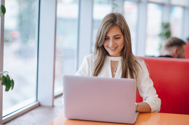 Mujer elegante con cara sonriente escribiendo en su portátil