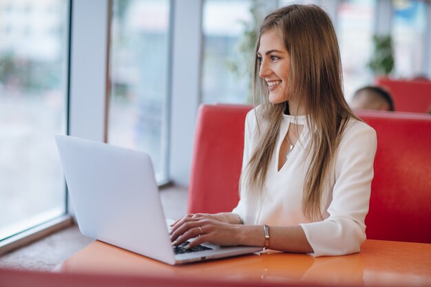 Mujer elegante con cara sonriente escribiendo en su portátil