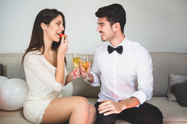 Mujer elegante comiendo una fresa mientras brinda con su novio