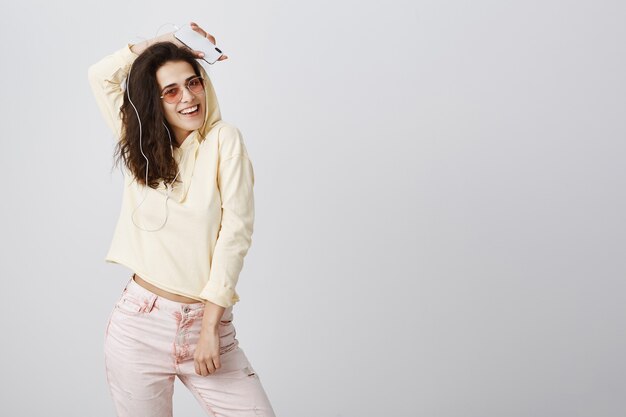 Mujer elegante despreocupada escuchando música con auriculares y bailando con el teléfono móvil