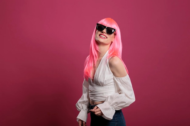 Mujer elegante y despreocupada con gafas de sol de moda en la cámara, sintiéndose segura y atractiva sobre un fondo rosa. Chica guapa sensual con lindas gafas en la cara, peinado funky.