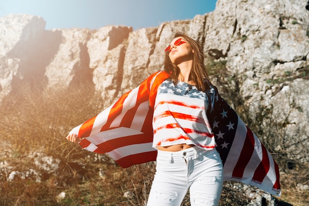 Mujer elegante envuelta en bandera americana en la naturaleza.