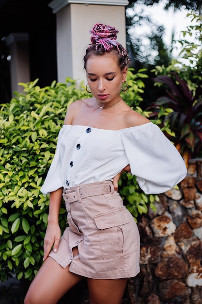 Mujer elegante europea con trenzas de verano de colores rosa en falda beige y blusa blanca