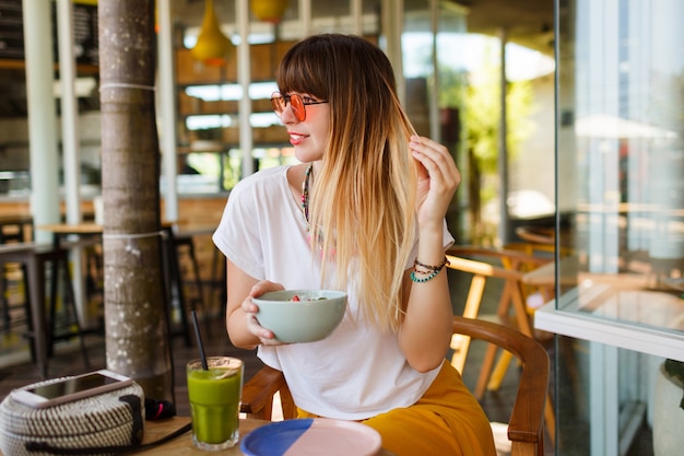 Foto gratuita mujer elegante feliz que come la comida sana que se sienta en el interior hermoso con las flores verdes