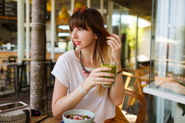 Mujer elegante feliz que come la comida sana que se sienta en el interior hermoso con las flores verdes