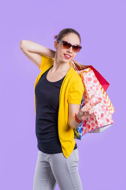 Mujer elegante feliz que muestra el signo de la paz mientras que sostiene el bolso de compras hermoso