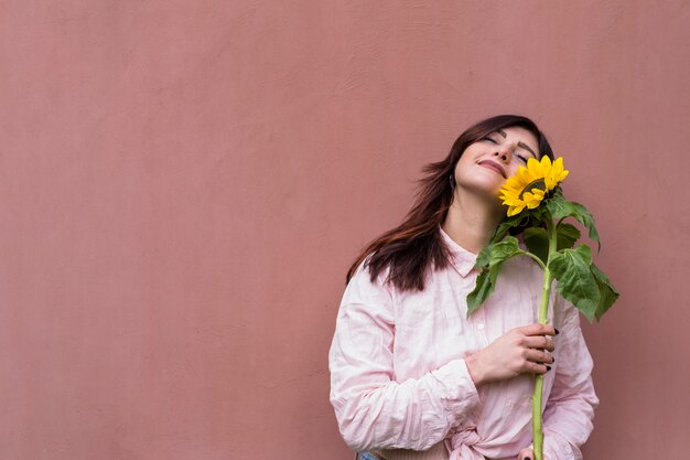 Mujer elegante con girasol en manos soñando alegremente