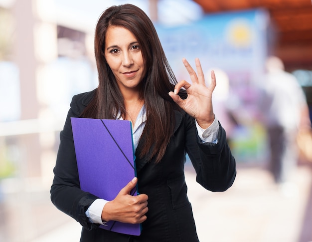 Mujer elegante haciendo ok con la mano y con una carpeta en la otra