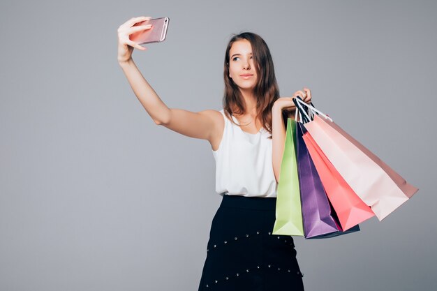 Mujer elegante haciendo selfie con bolsas de la compra sobre fondo blanco con bolsas de papel en sus brazos