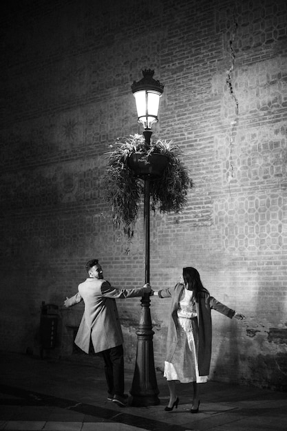 Mujer elegante y hombre sonriente joven que gira alrededor de la lámpara de calle iluminada