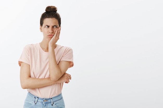 Mujer elegante joven confundida y disgustada posando contra la pared blanca