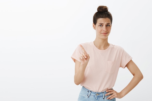 Mujer elegante joven sin divertirse posando contra la pared blanca