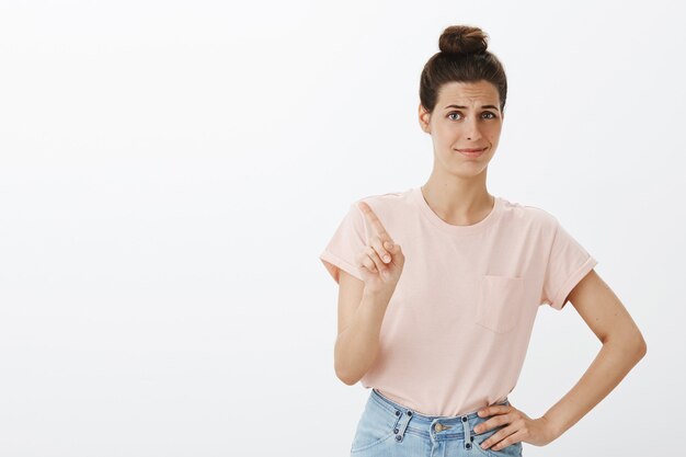 Mujer elegante joven sin divertirse posando contra la pared blanca