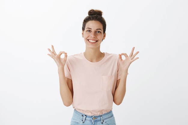 Mujer elegante joven satisfecha y complacida posando contra la pared blanca