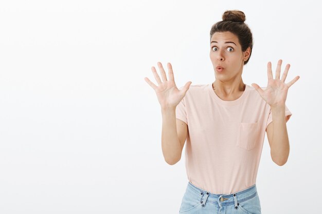 Mujer elegante joven sorprendida posando contra la pared blanca