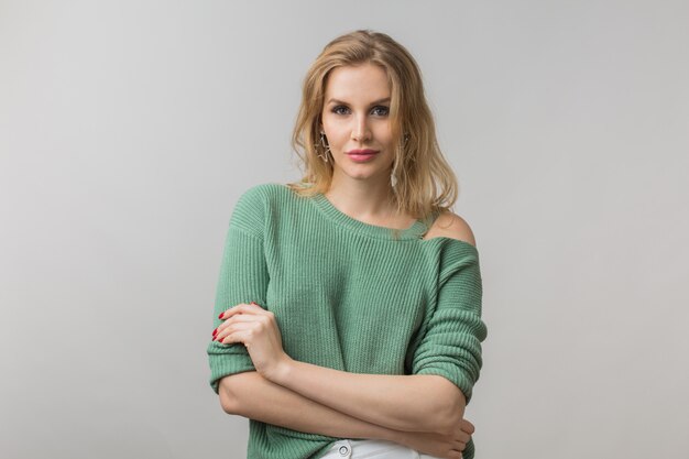 Mujer con elegante maquillaje y suéter verde posando en rosa