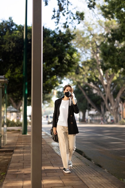 Foto gratuita mujer elegante con una máscara médica afuera y hablando por teléfono